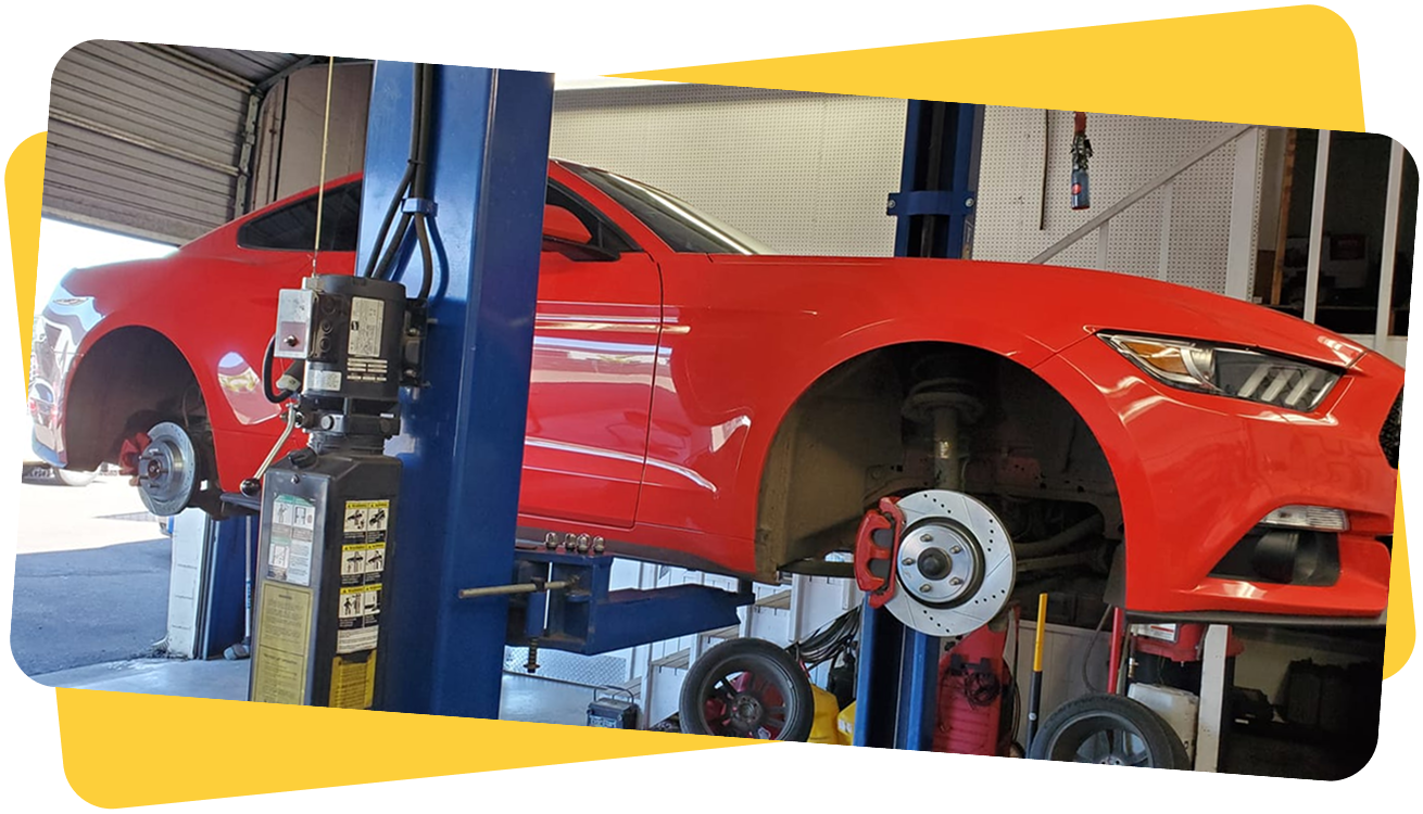 A red car is sitting on a lift in a garage. | Auto Team Service Center