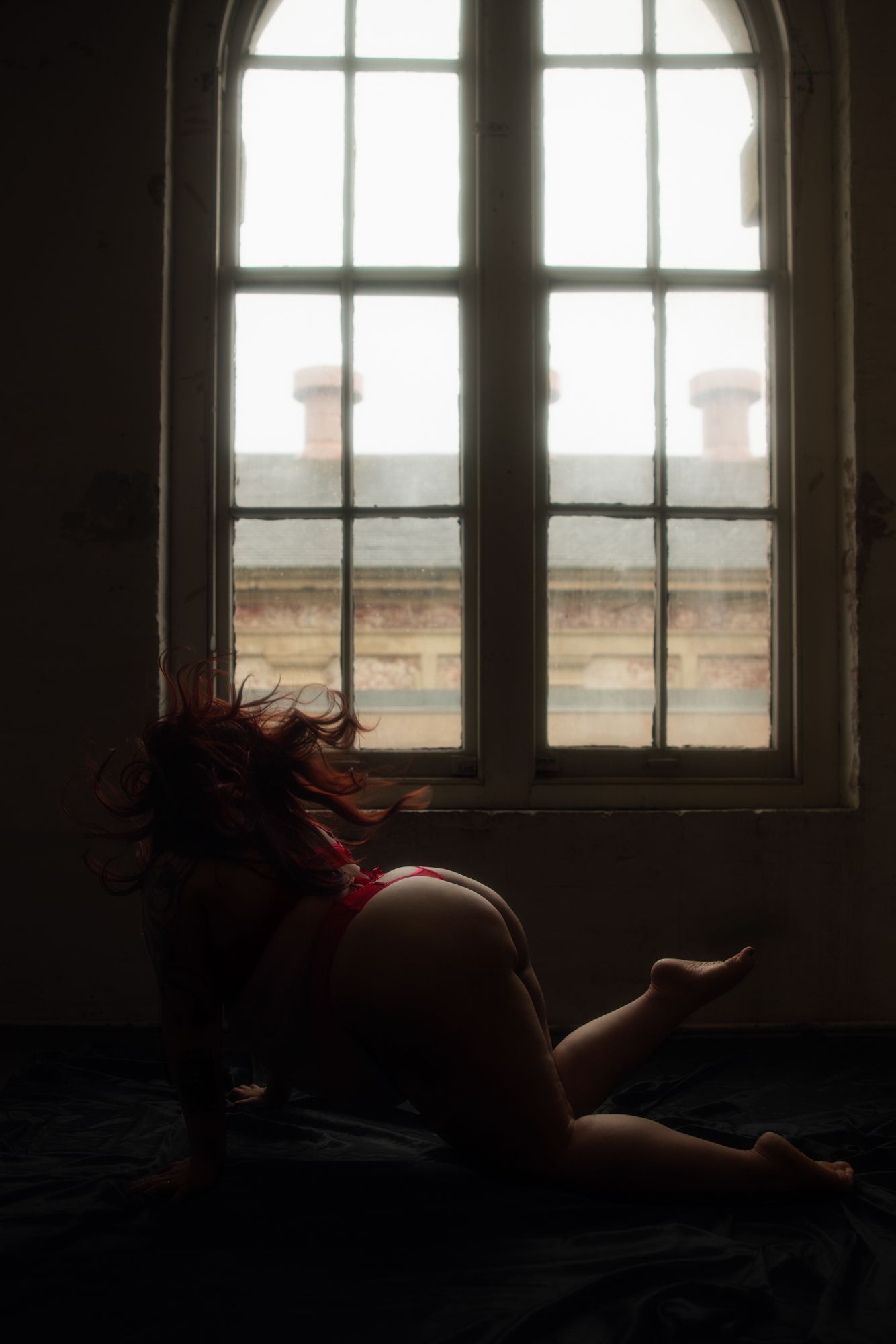 Woman in red bodysuit arches back in front of a window; her silhouette is visible.