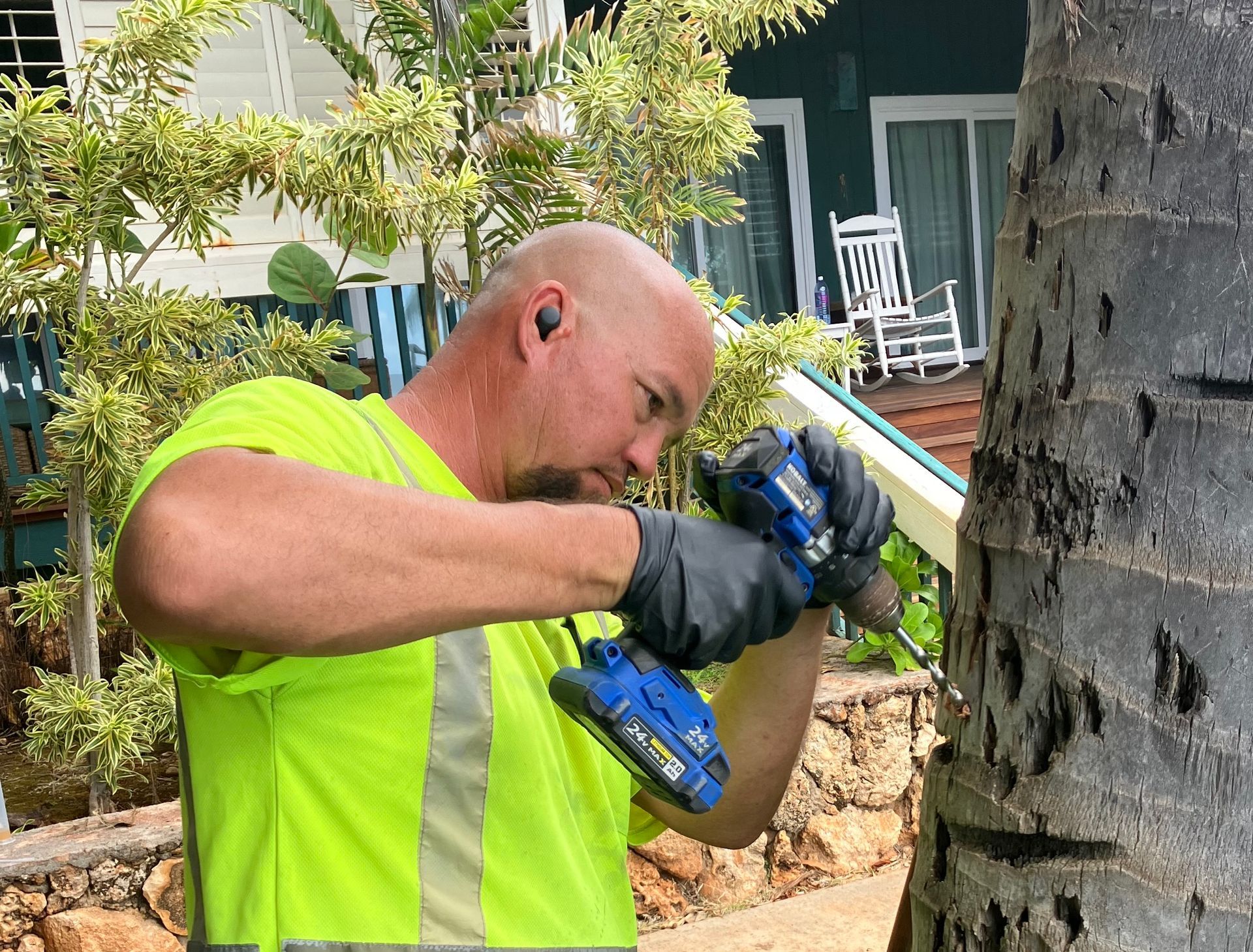 Worker in neon yellow shirt drilling into a brick wall outdoors near a house.