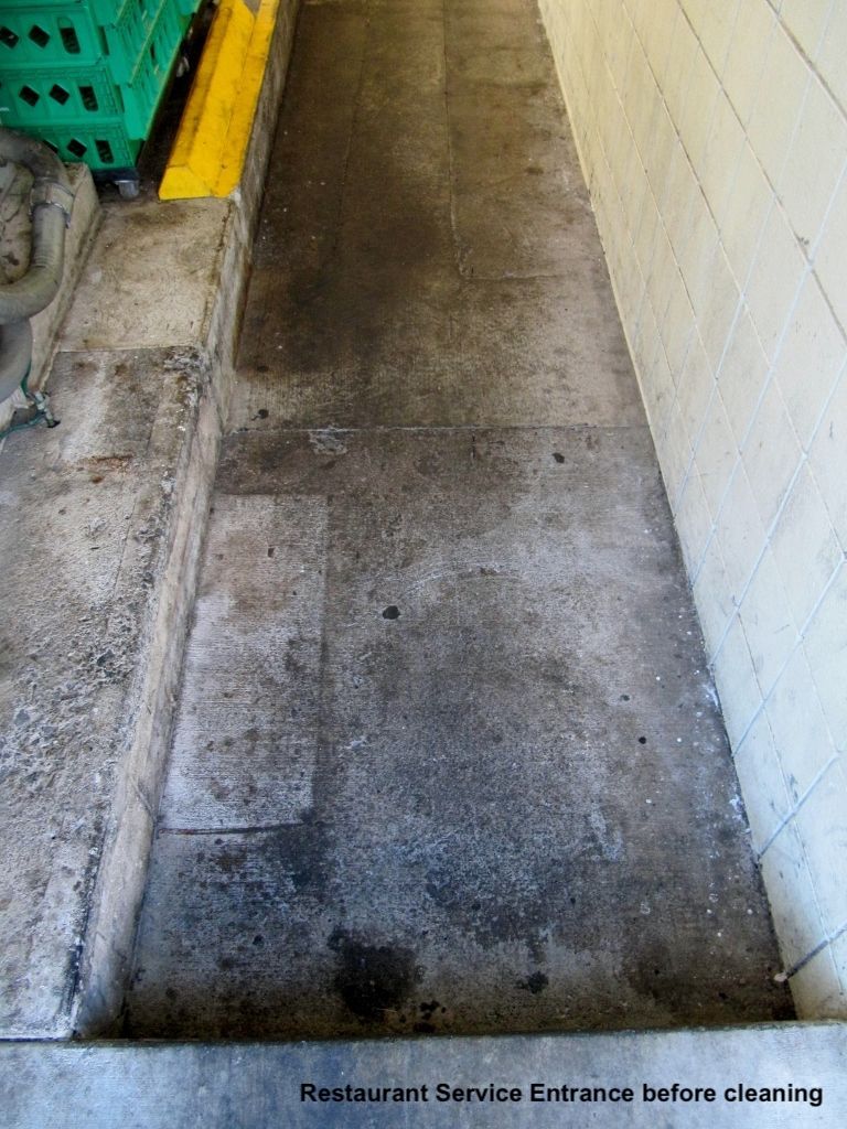 Narrow concrete walkway beside a wall and utility area, showing dark stains and worn flooring before cleaning