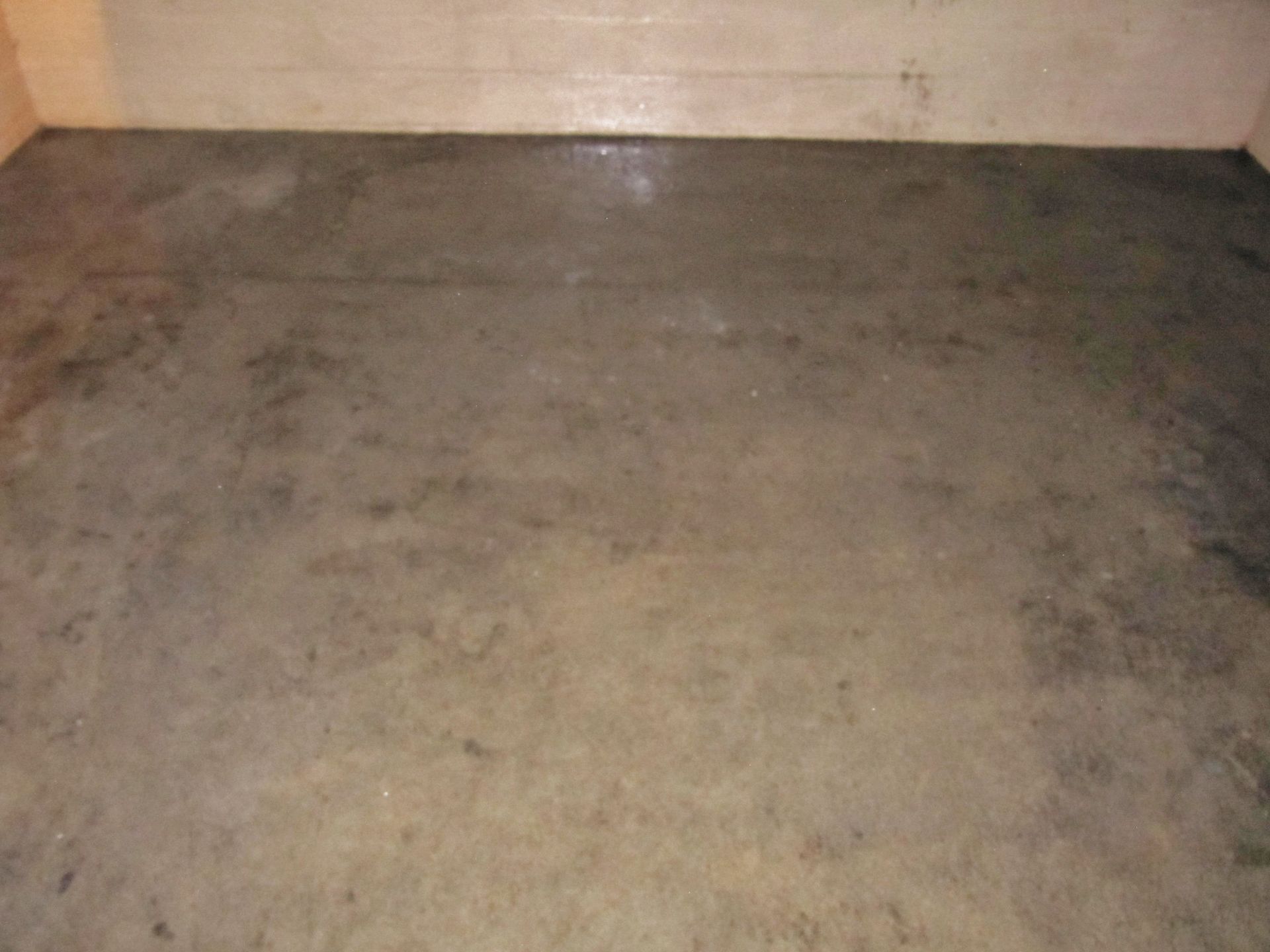 Empty concrete floor in a bare room with beige walls and a dark corner.