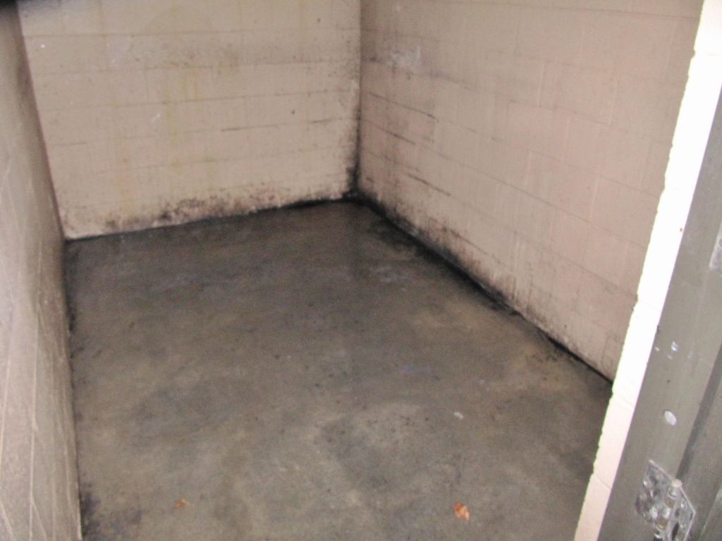 Empty dirty tiled corner of a small room with a stained concrete floor