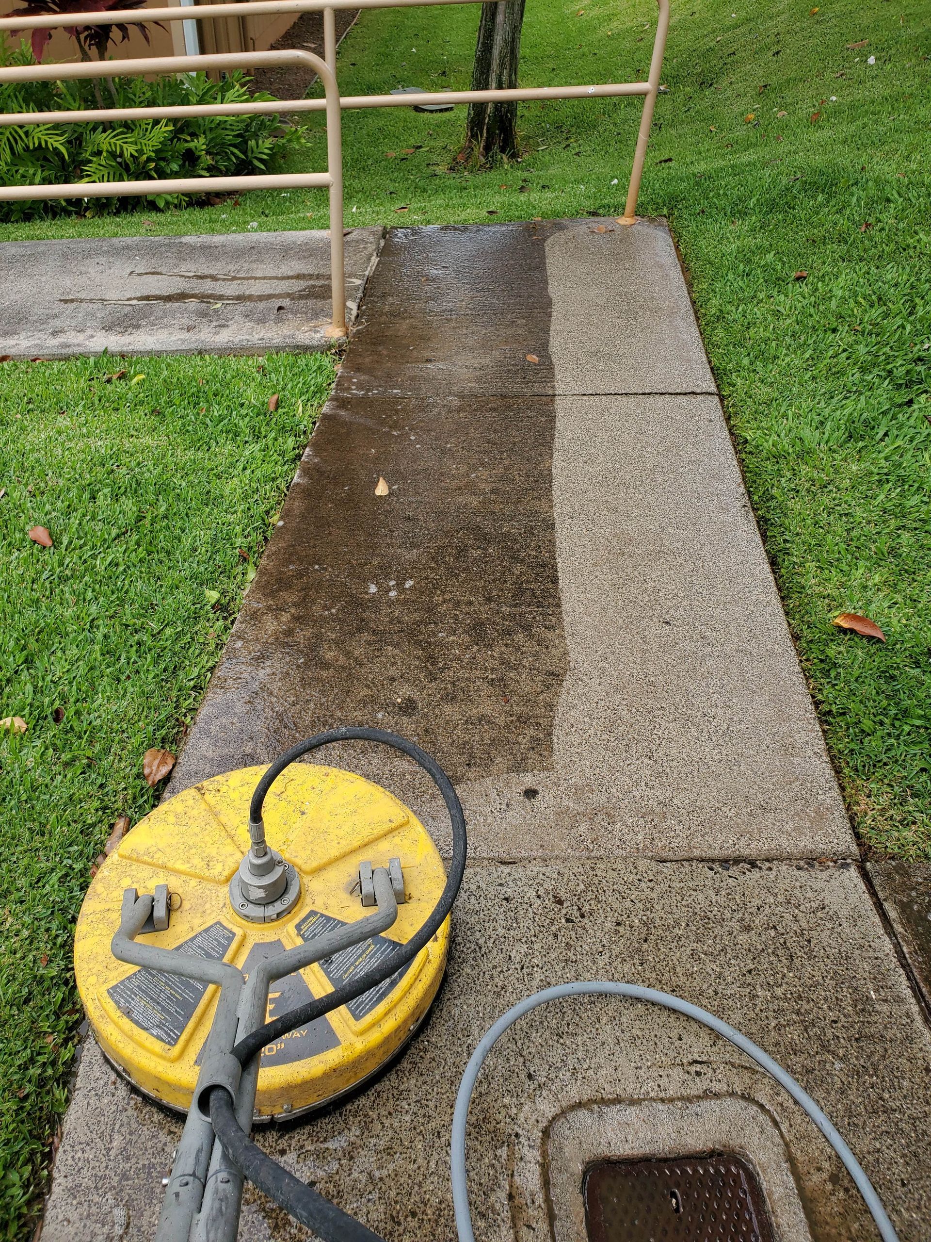 Yellow pressure washer on a wet concrete walkway beside grass and a metal gate