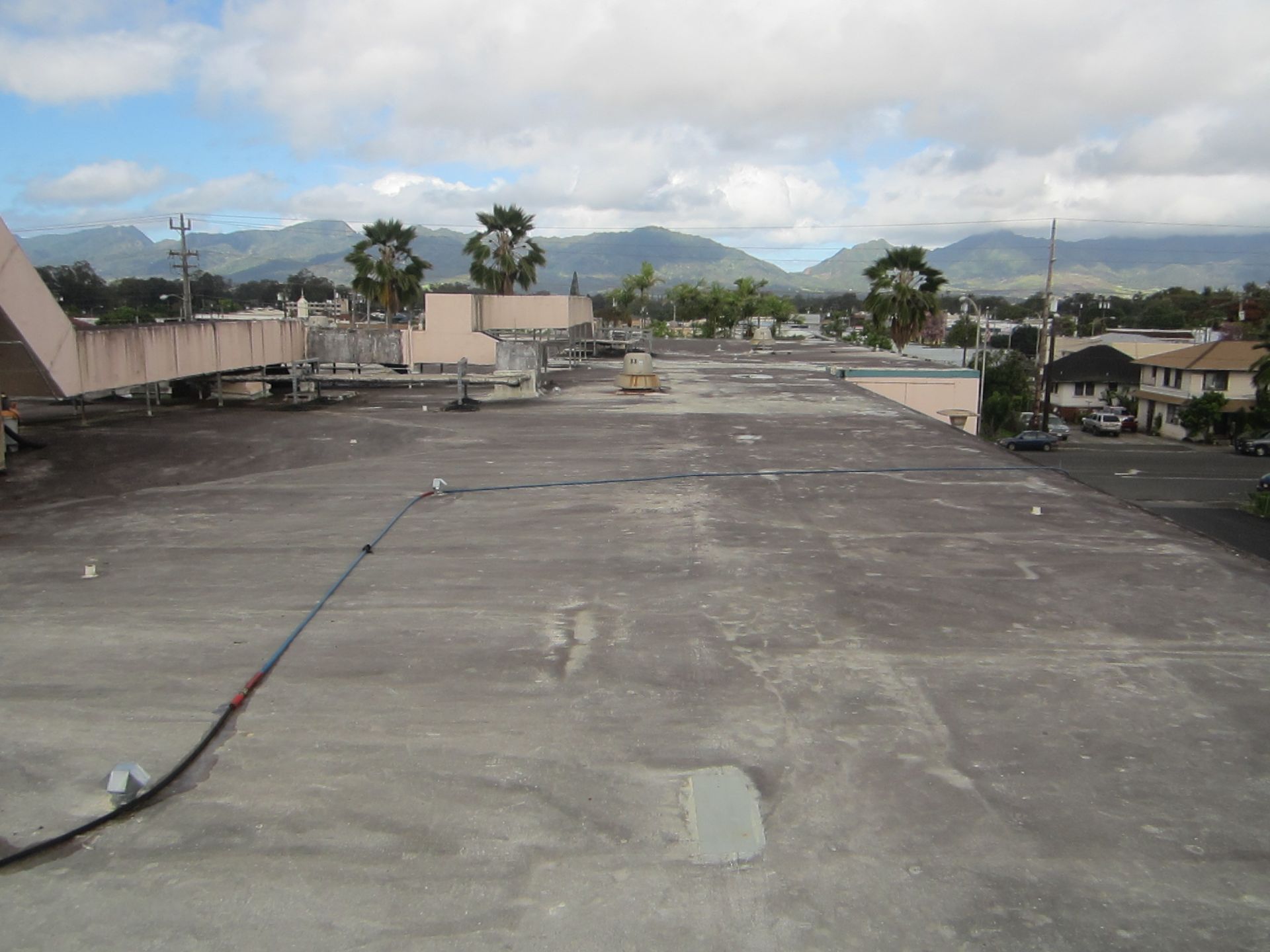 Rooftop parking area with mountain view, palm trees, and cloudy sky in the distance