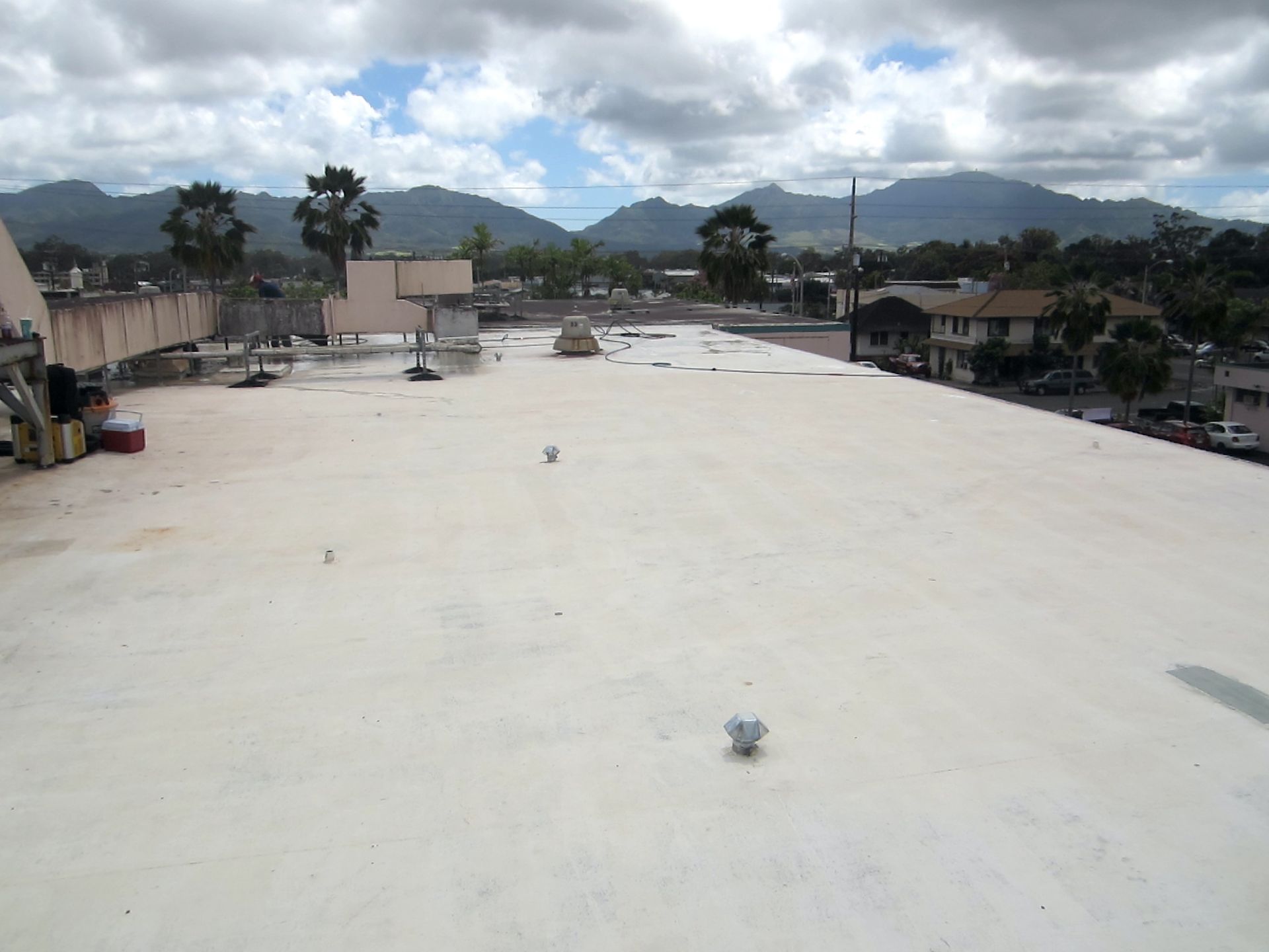 Wide white rooftop with scattered vents, overlooking a town and mountains under a cloudy sky.
