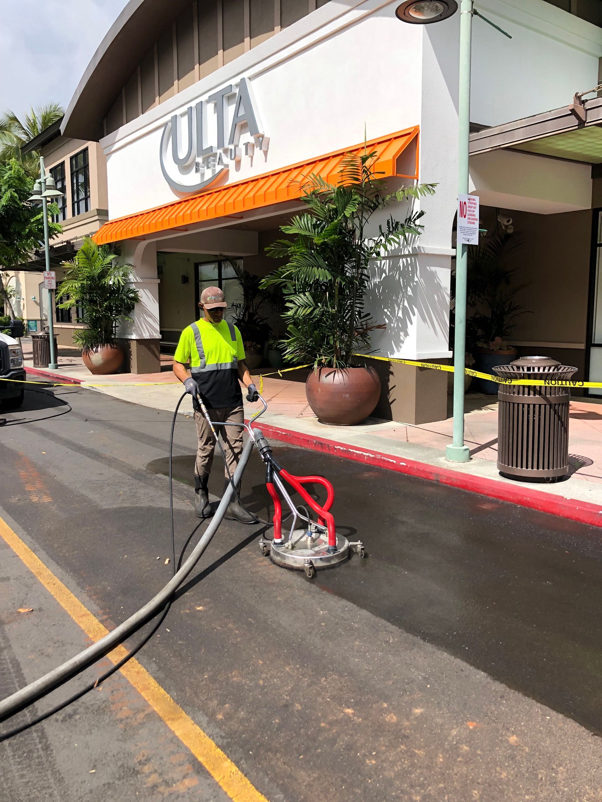 A person in a high-visibility vest uses a surface cleaner to wash the pavement in front of an Ulta Beauty store.