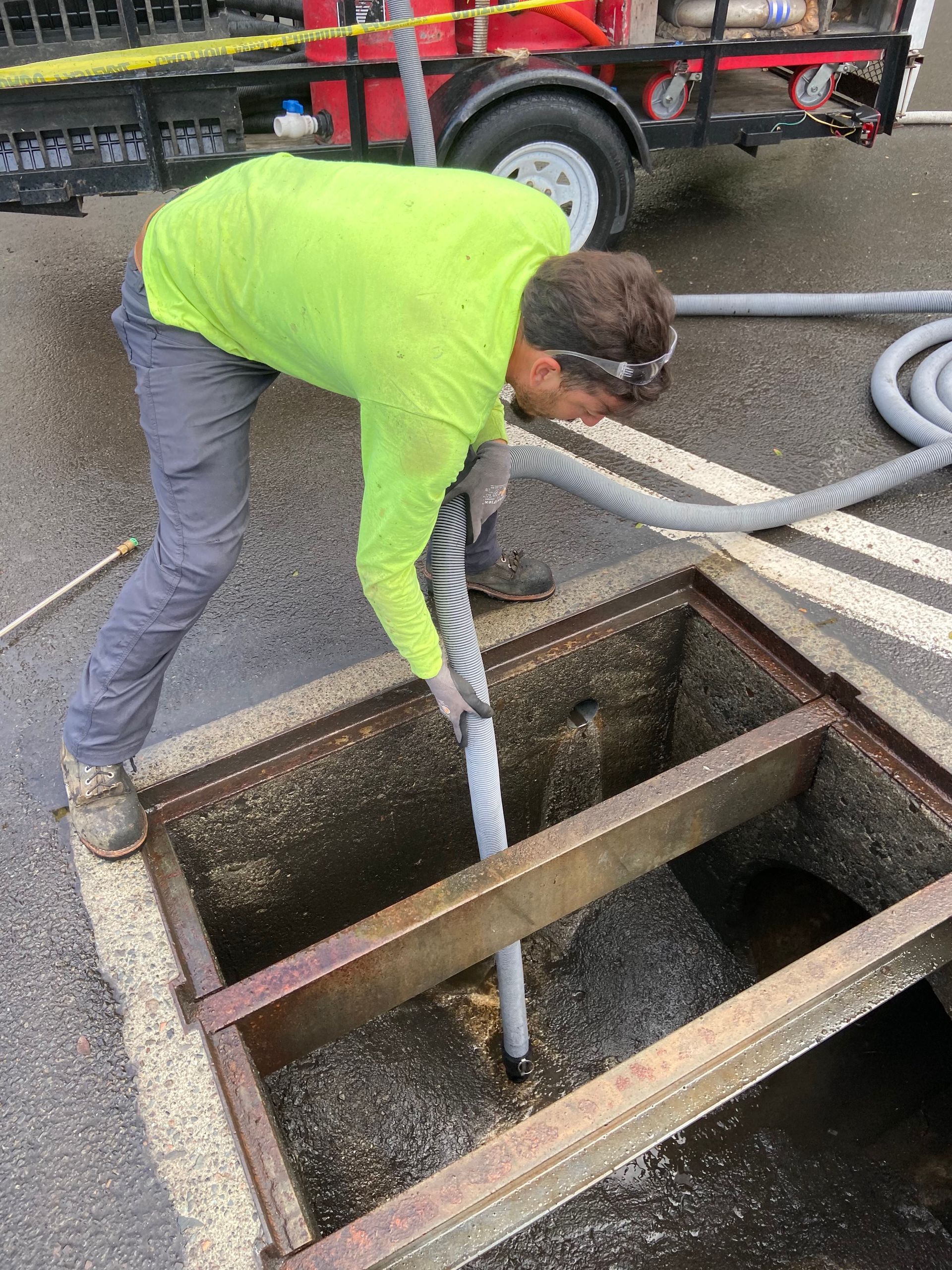 Worker in a neon green shirt leaning into a manhole, handling a hose near a truck.