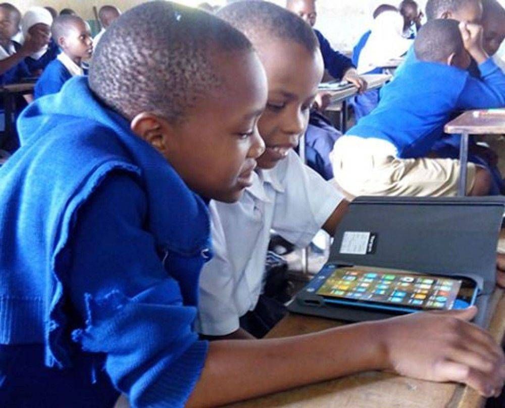 A group of children are sitting in a classroom looking at a tablet.