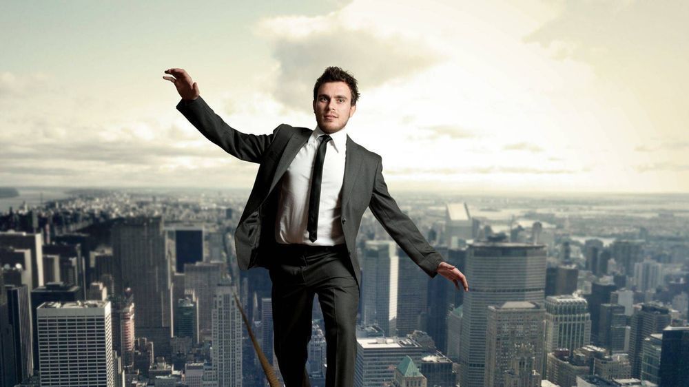 A man in a suit and tie is balancing on a rope over a city.