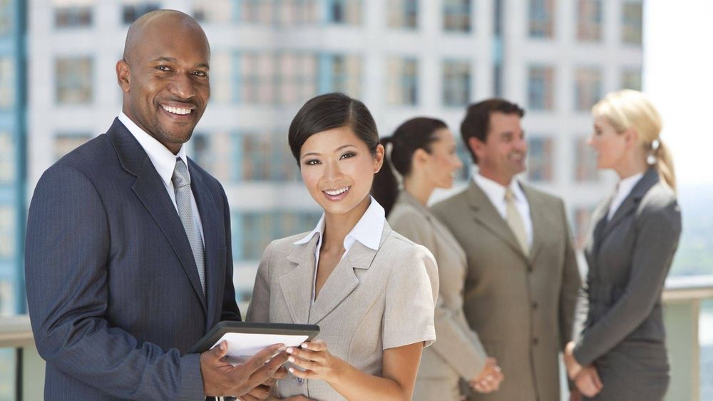 A man and a woman are standing next to each other in front of a group of business people.