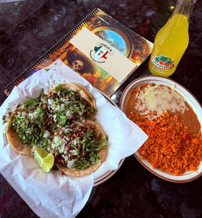 A taco and a plate of rice are on a table next to a menu