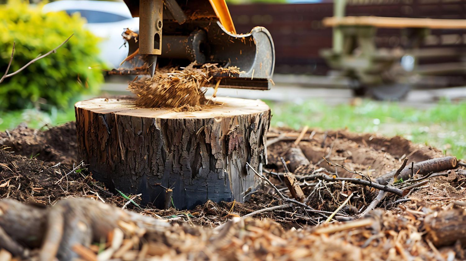 A mechanical stump grinder cuts into a tree stump surrounded by wood chips in a backyard setting.