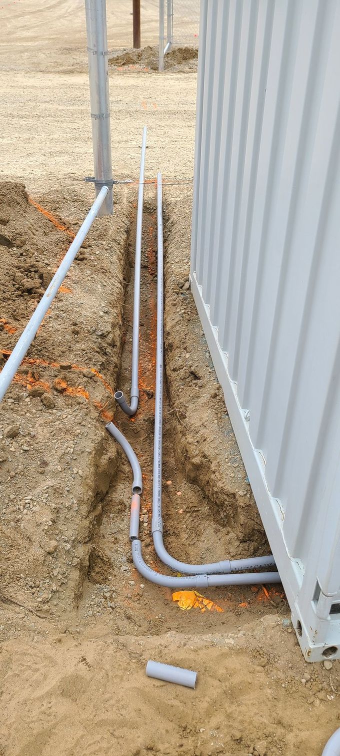 An open trench next to a container reveals buried electrical conduits.