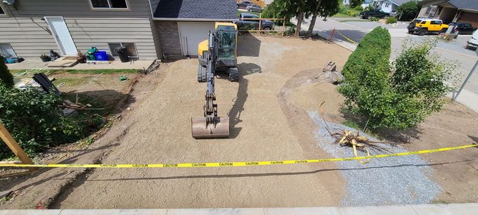 Construction site with an excavator on a gravel driveway, surrounded by caution tape.