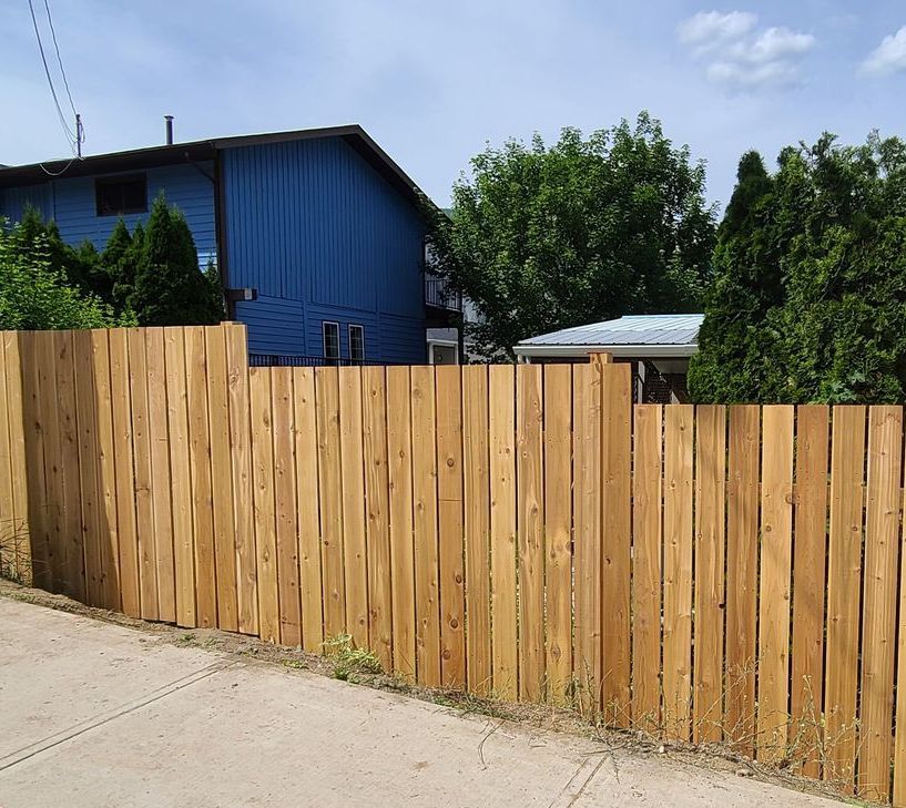 Wooden fence in front of a blue building on a sunny day.