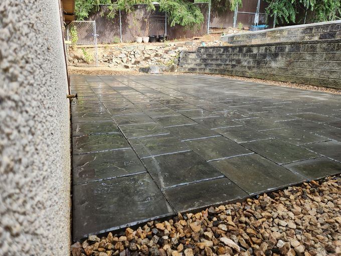 Stone patio adjacent to a pebbled area, retaining wall in background, overcast day.
