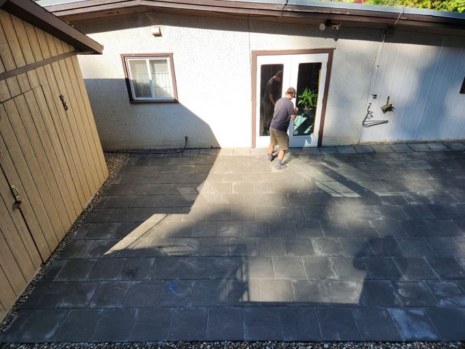 A person exits a white door onto a stone patio, a wooden shed is on the left.