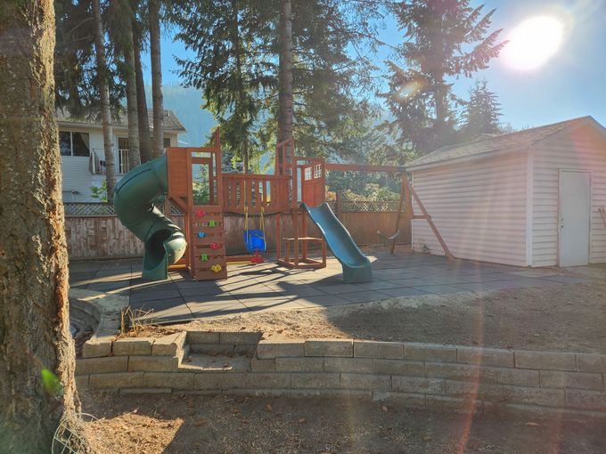 Playground with slides and climbing wall, next to a shed, in a yard.