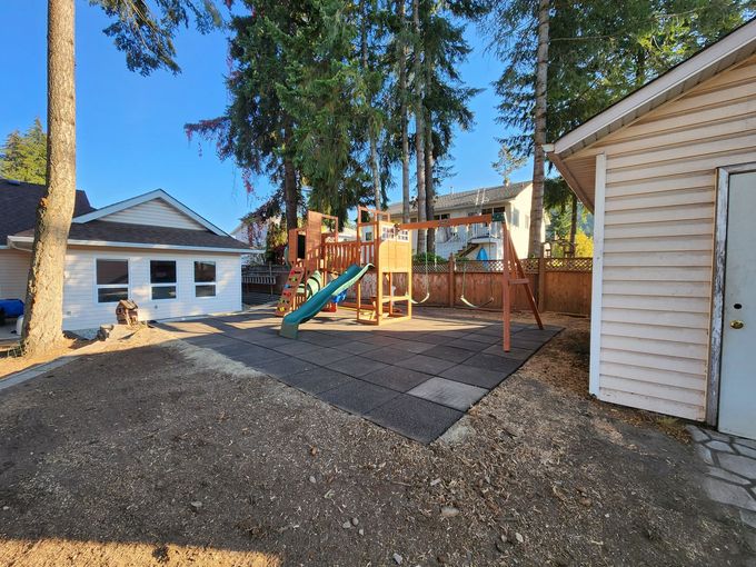 Playground in a backyard, with swings, a slide, and wood-chip ground cover. Buildings and trees in the background.