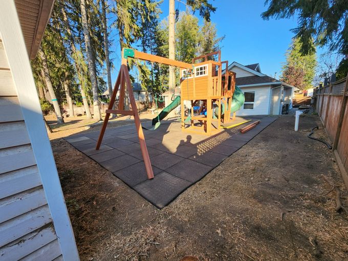 Playground set on rubber tiles in a backyard. Swing set and climbing structure with slide.