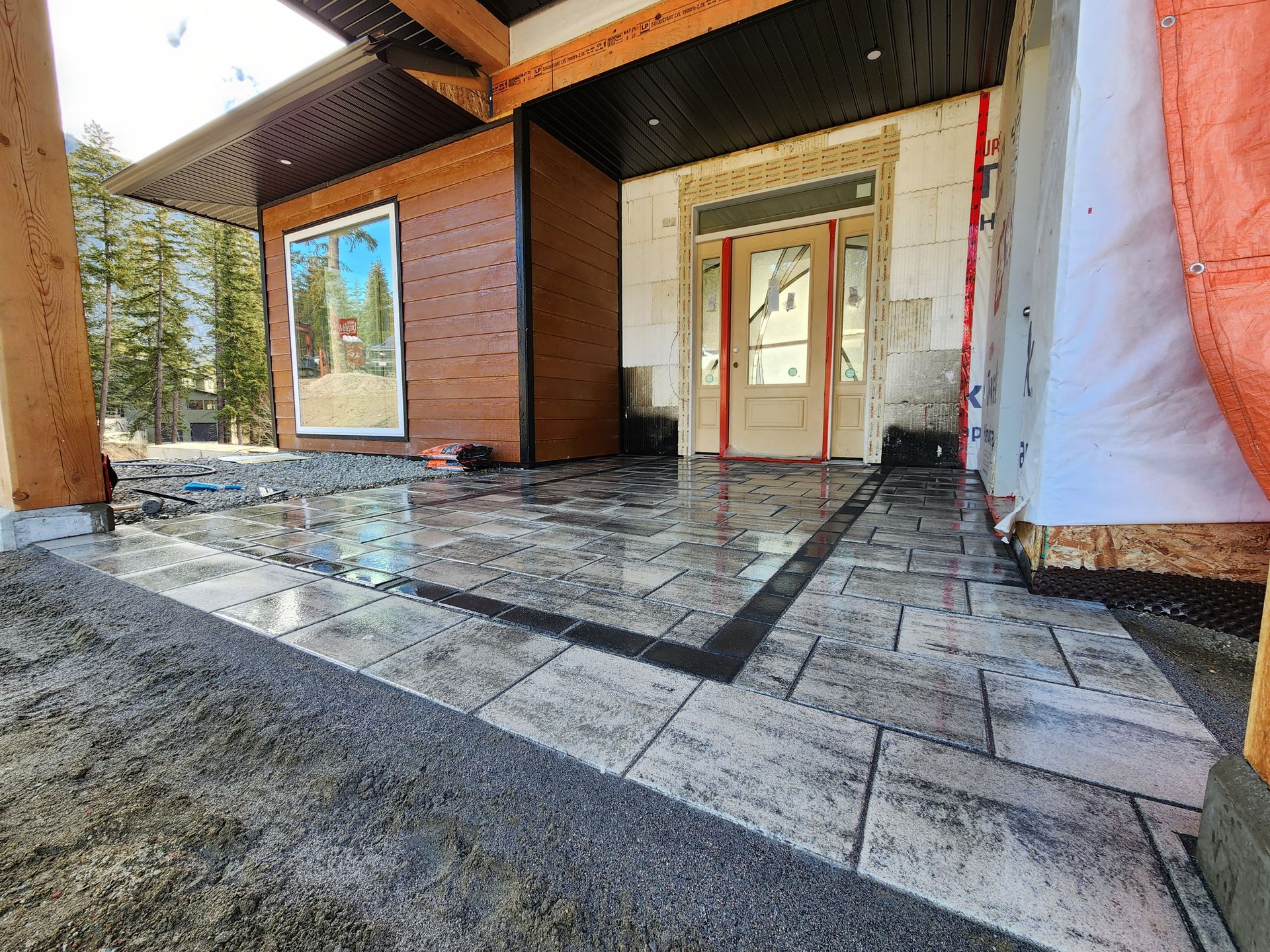 A newly constructed patio with gray pavers, a dark border, and a partially visible house front.