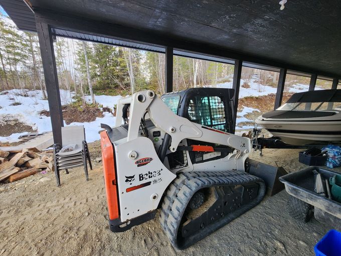 Bobcat E88 compact track loader under a covered structure, next to a boat, with snow.
