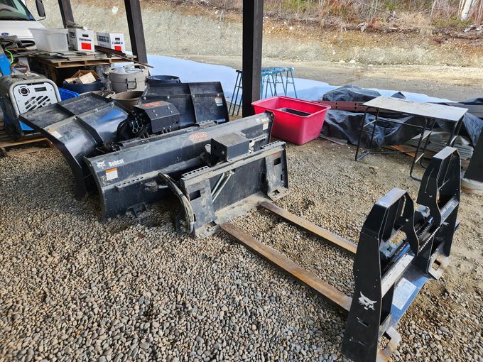 Bobcat attachments: snowblower, pallet forks, and a power generator sit outdoors under a roof on gravel.