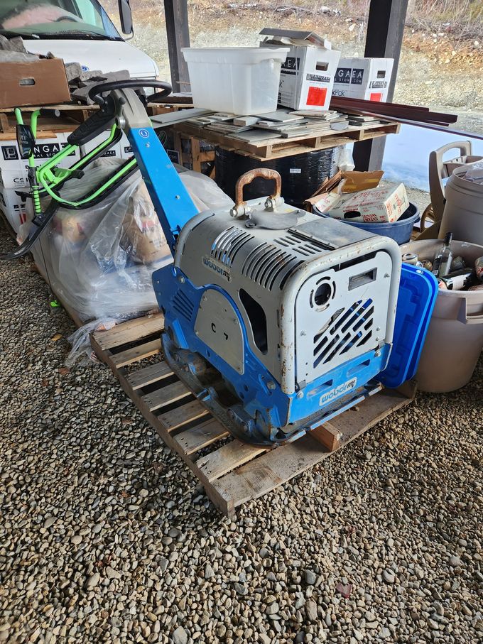 Blue and gray plate compactor on a wooden pallet, outside.