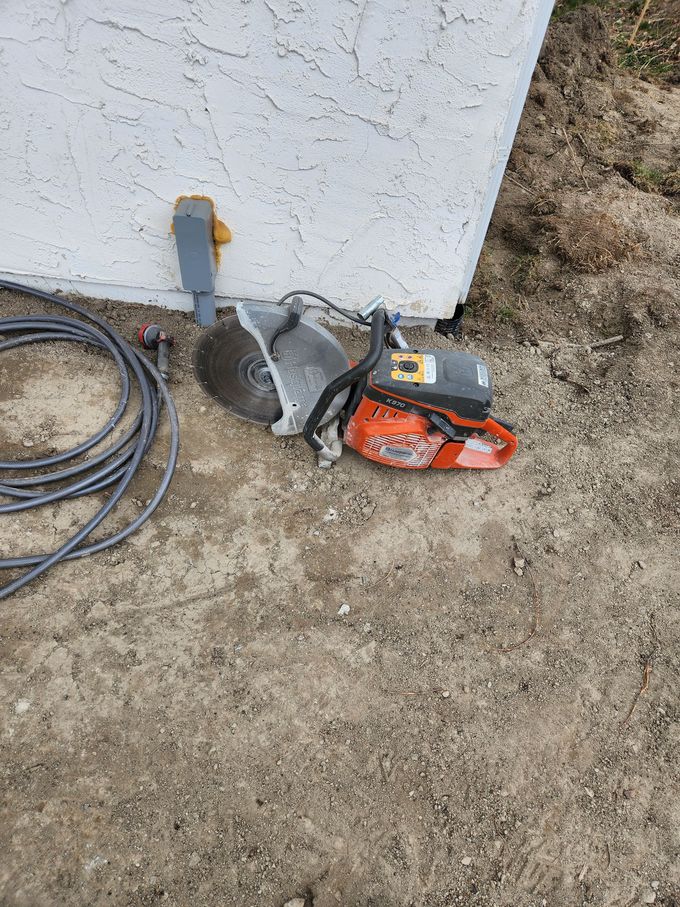Chainsaw and circular saw lying on dirt next to a building's stucco wall.