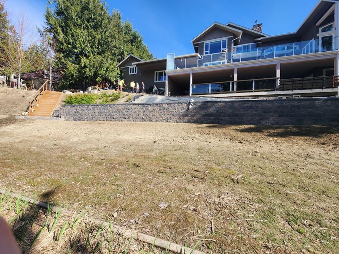Large house with retaining wall and barren yard on a sunny day.