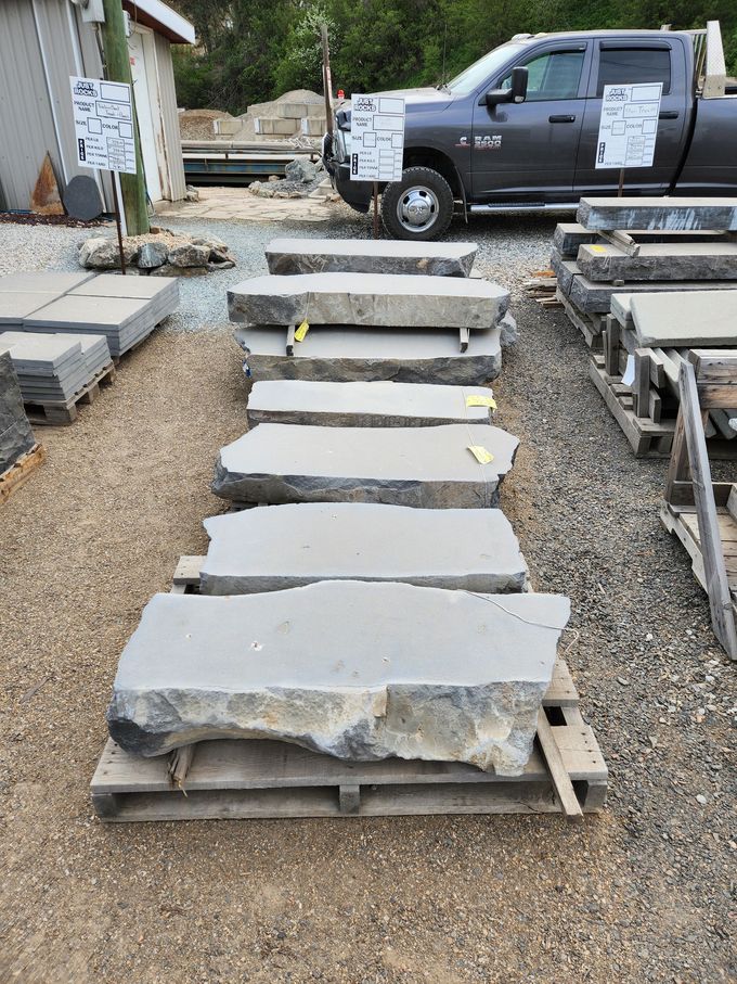 Stone steps on a pallet in a yard. Gray truck in background. Gravel ground.