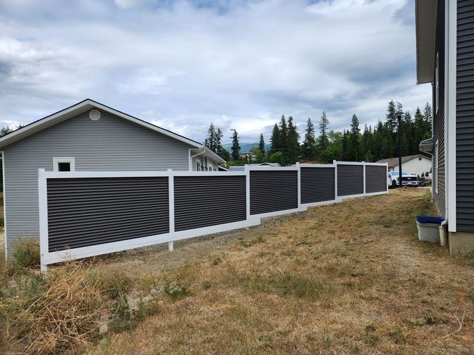White fence with decorative panels in a yard with a garage and house on a cloudy day.