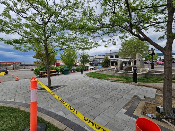 A paved outdoor area with trees and caution tape. Buildings are in the background.