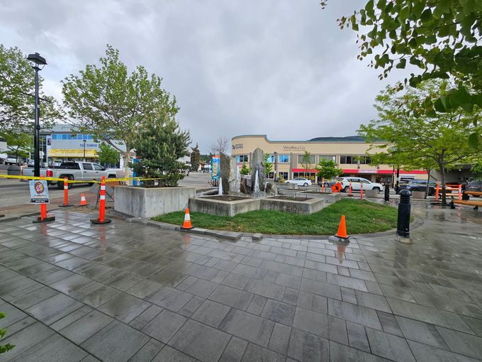 A town square with a fountain under a cloudy sky. Orange cones surround the fountain.