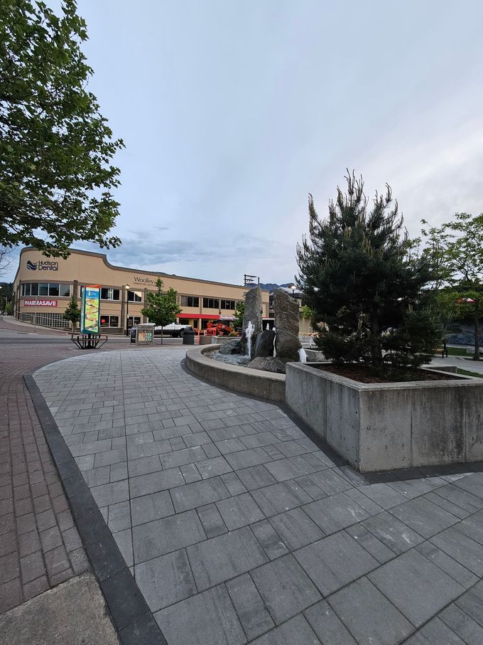 Paved town square with a fountain and a building in the background under a cloudy sky.