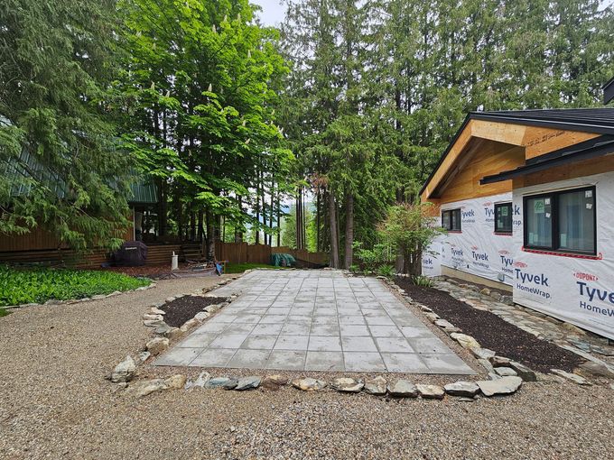 A concrete patio outside a house under construction, surrounded by landscaping and trees.