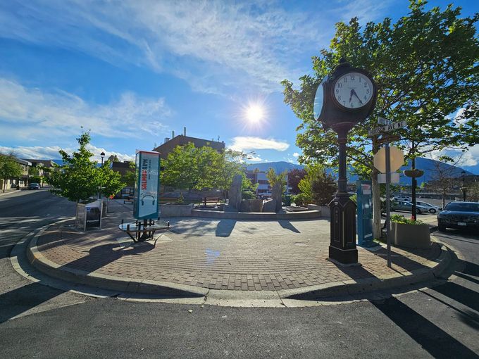 A sunny town square with a clock tower, trees, and a blue sky.