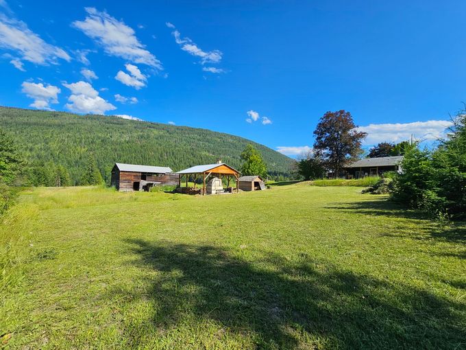 Grassy field with old wooden structures, under a bright blue sky and mountain backdrop.