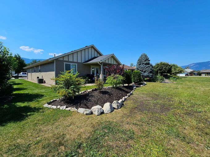 A one-story house with a well-maintained garden, green grass, and a mountain backdrop on a sunny day.