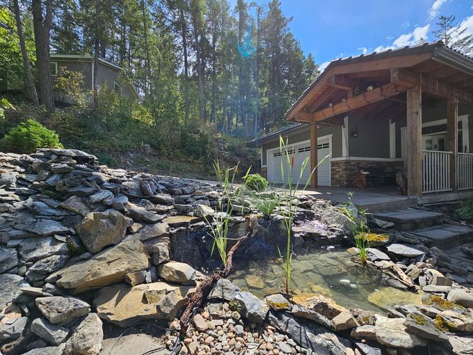 A rustic home with a small pond cascading over rocks; sunny day in a wooded setting.