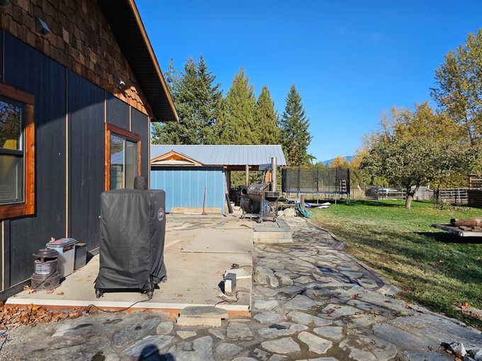 Backyard with house, grill, shed, trampoline, trees, and blue sky.