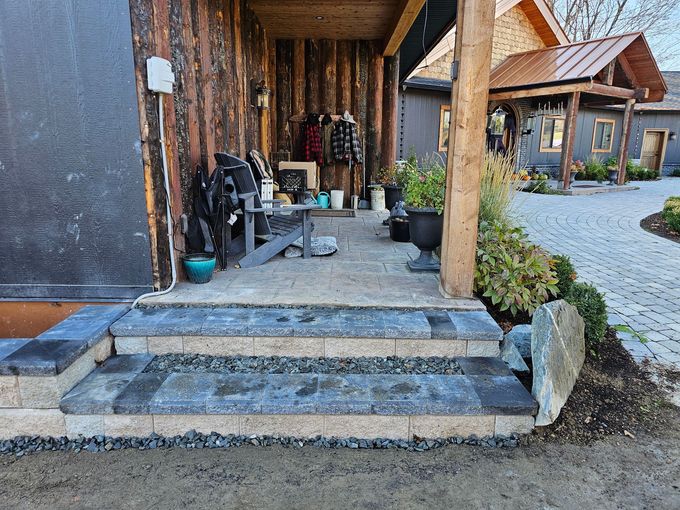 Stone steps leading to a porch with coats and plants, next to a building with wooden siding.