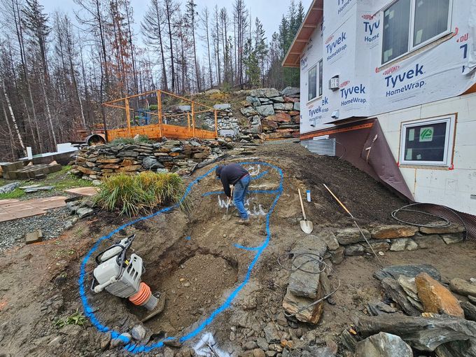 Man excavating a marked area on a hillside, near a house under construction.