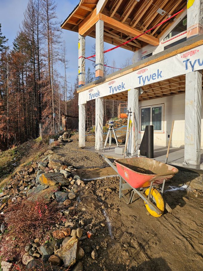 Construction site; house with large columns. A wheelbarrow of dirt sits on a hillside with rocky terrain.