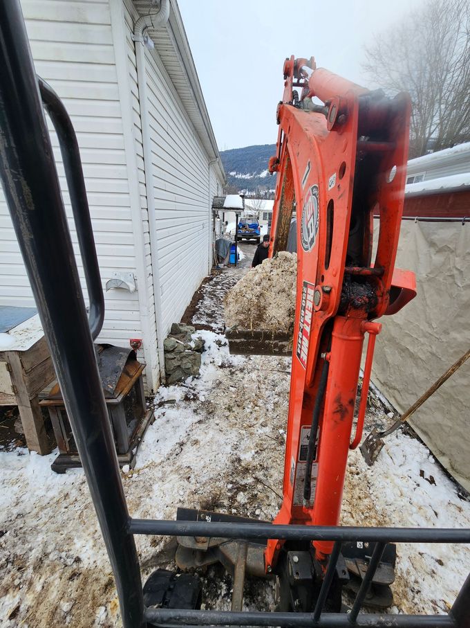 Orange excavator digging snow alongside a white building. Winter scene.