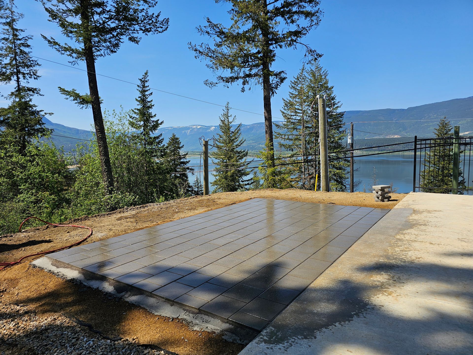 Concrete pad with drainage grooves, overlooking a lake and mountains under a sunny sky.