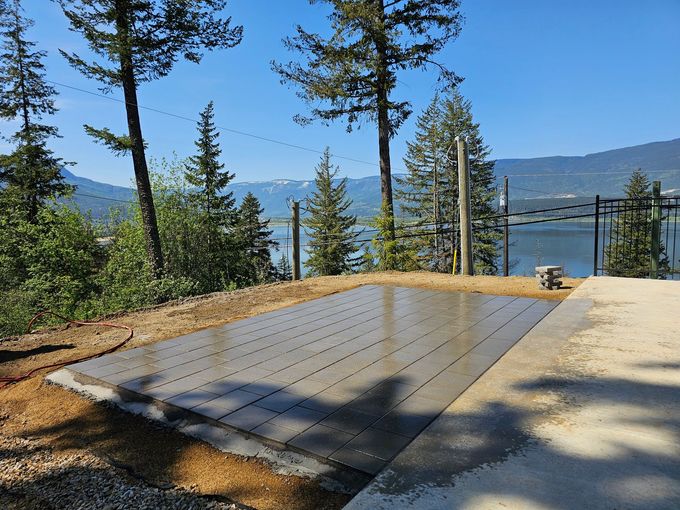 Concrete pad with drainage grooves, overlooking a lake and mountains under a sunny sky.