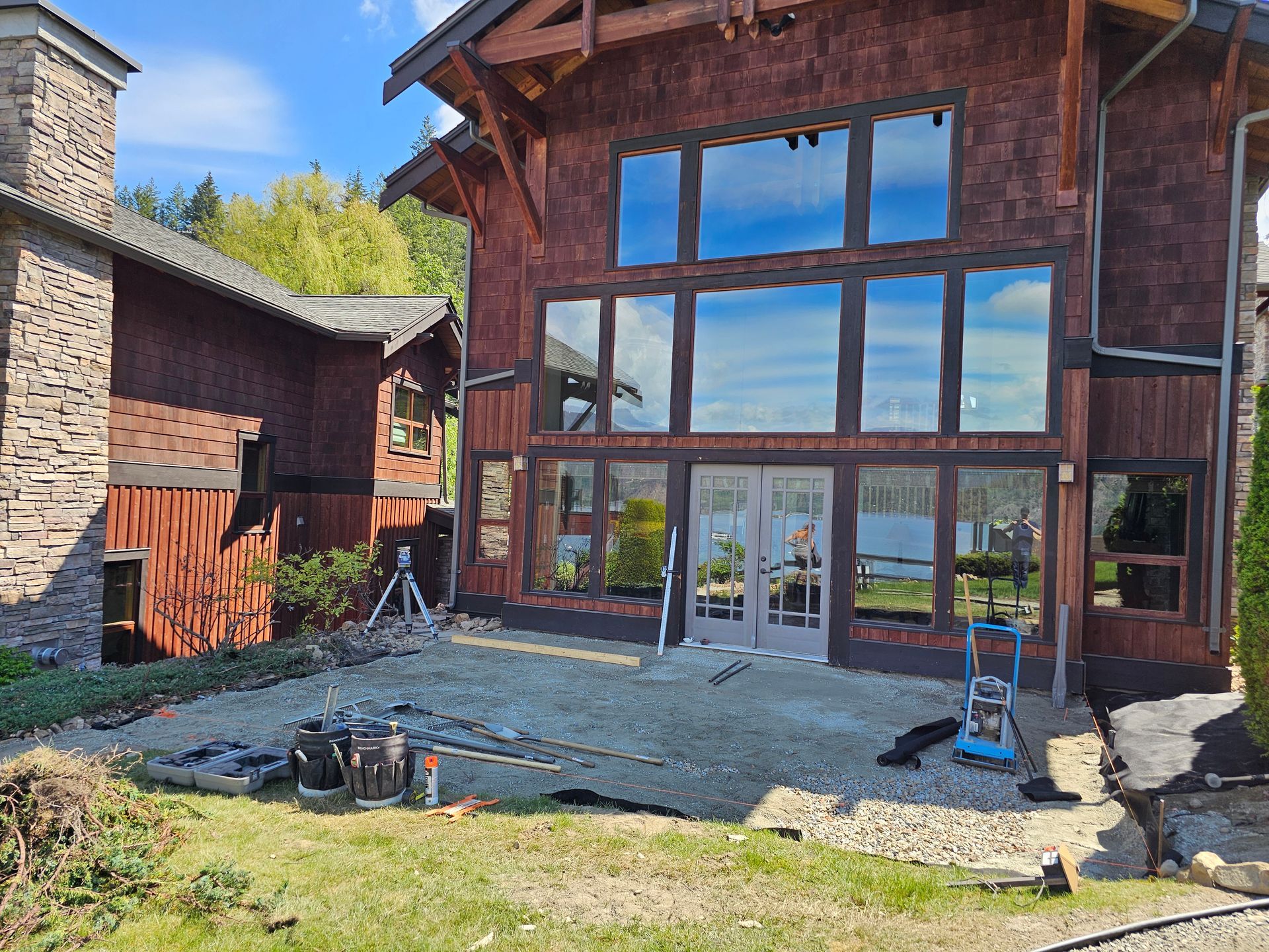 Cedar-sided house with large windows; patio under construction, blue sky reflected in glass.