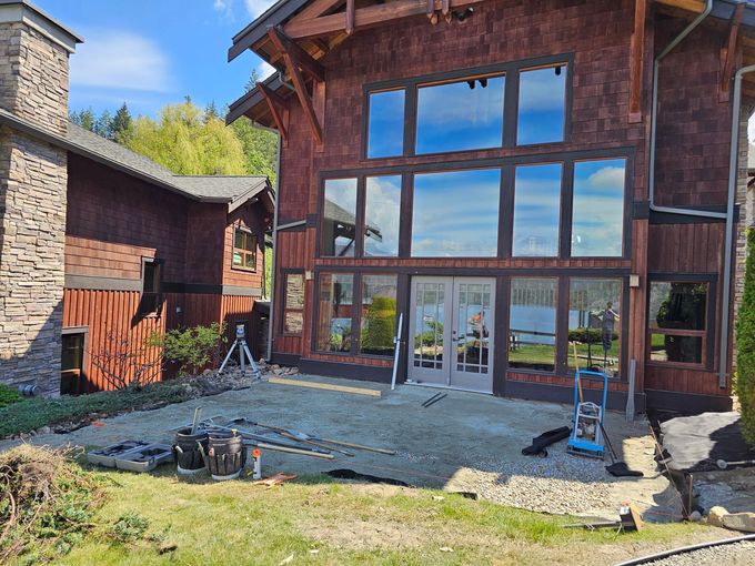 Cedar-sided house with large windows; patio under construction, blue sky reflected in glass.