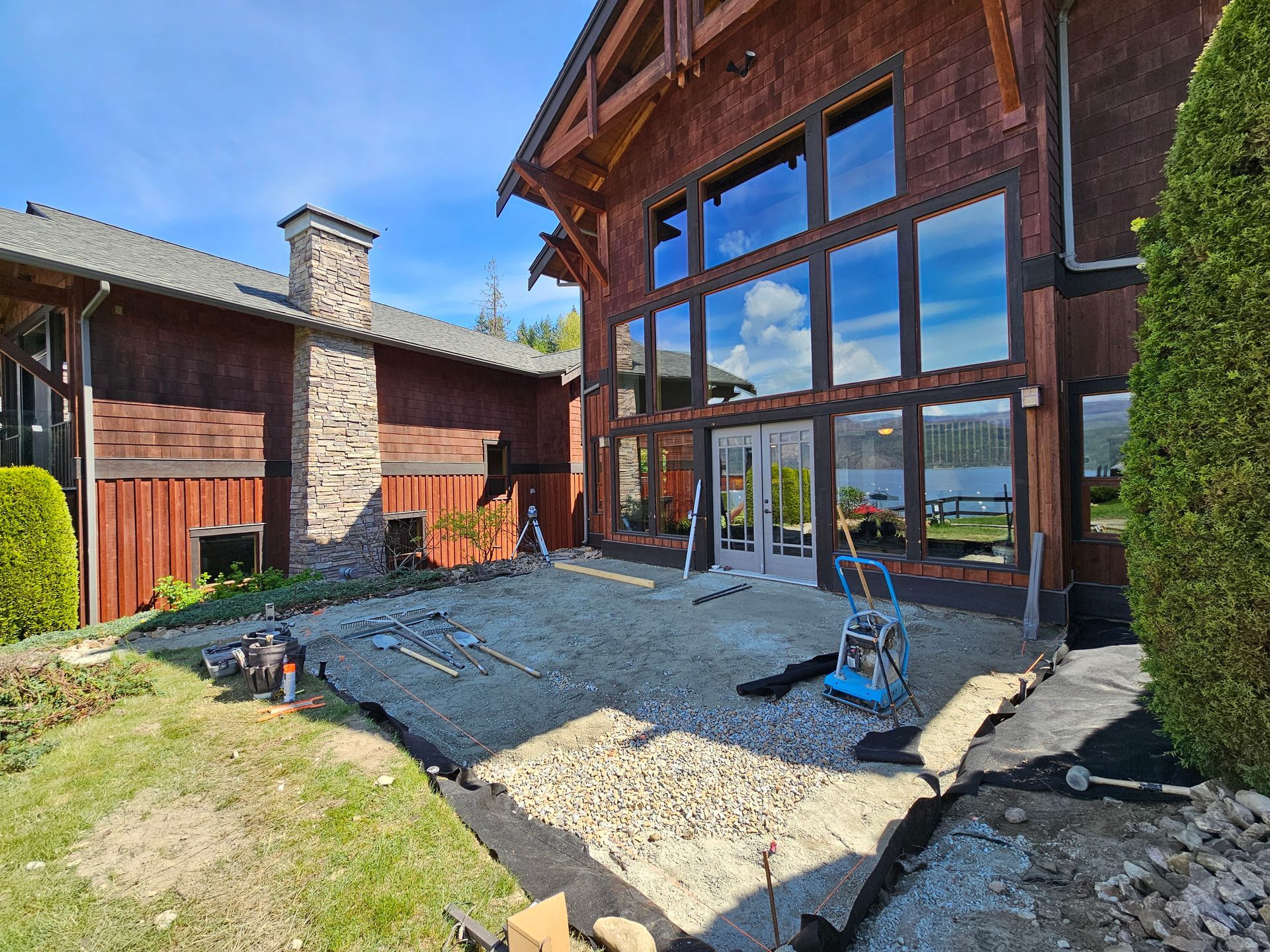 Exterior of a house with a gravel patio under construction, overlooking a lake.